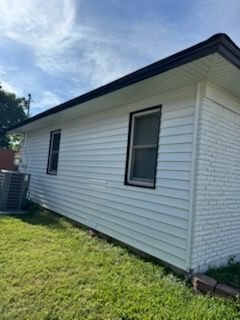 Side of a white house with dark trim, two windows, and green lawn under a blue sky.