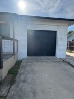 Concrete driveway leading to a dark garage door on a white house exterior.
