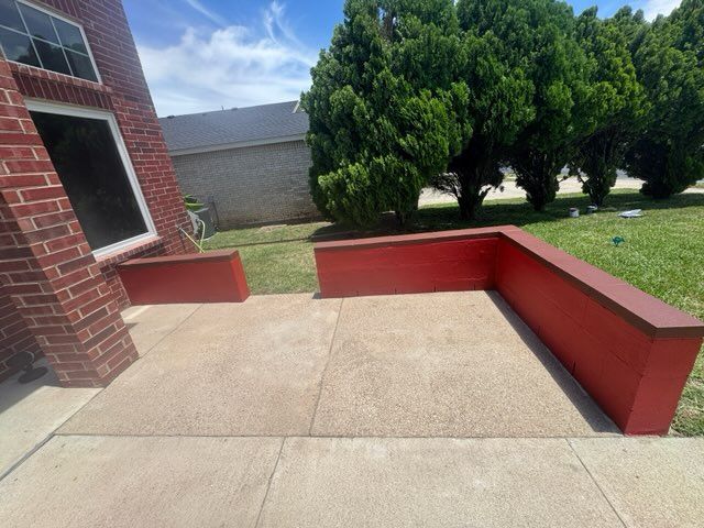 Concrete patio with red brick planters beside a house, trees and lawn in the background