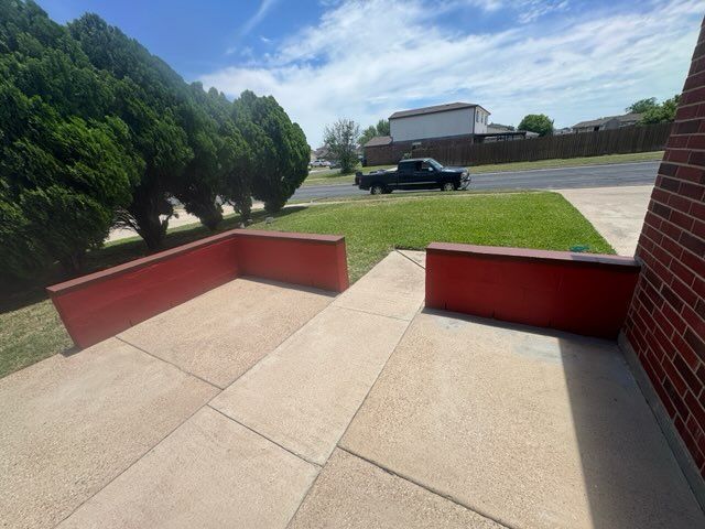 Concrete walkway beside red brick walls, overlooking a grassy lot with a black pickup truck and trees.