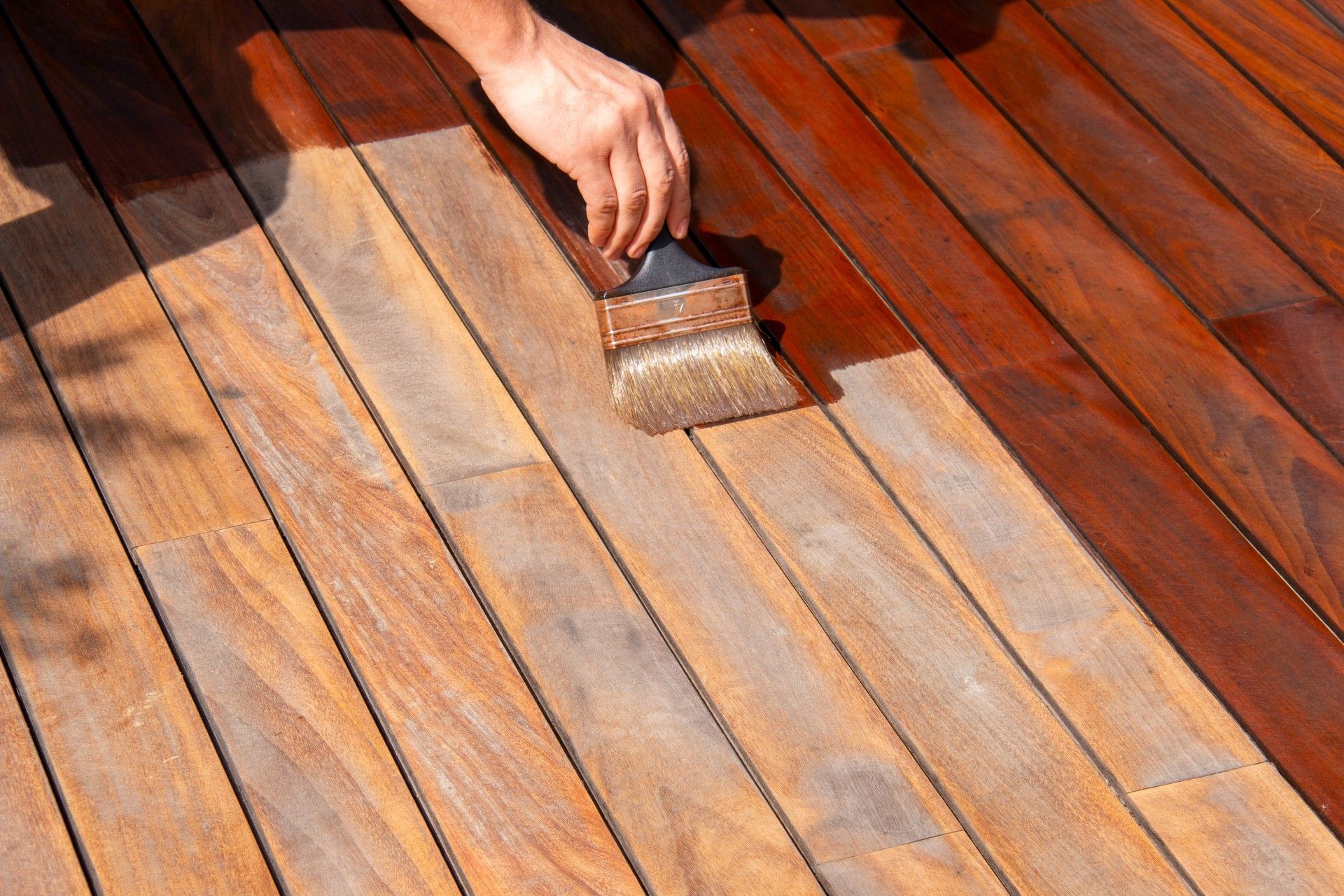 Hand brushing varnish onto a wooden floorboards surface, showing a glossy finish area