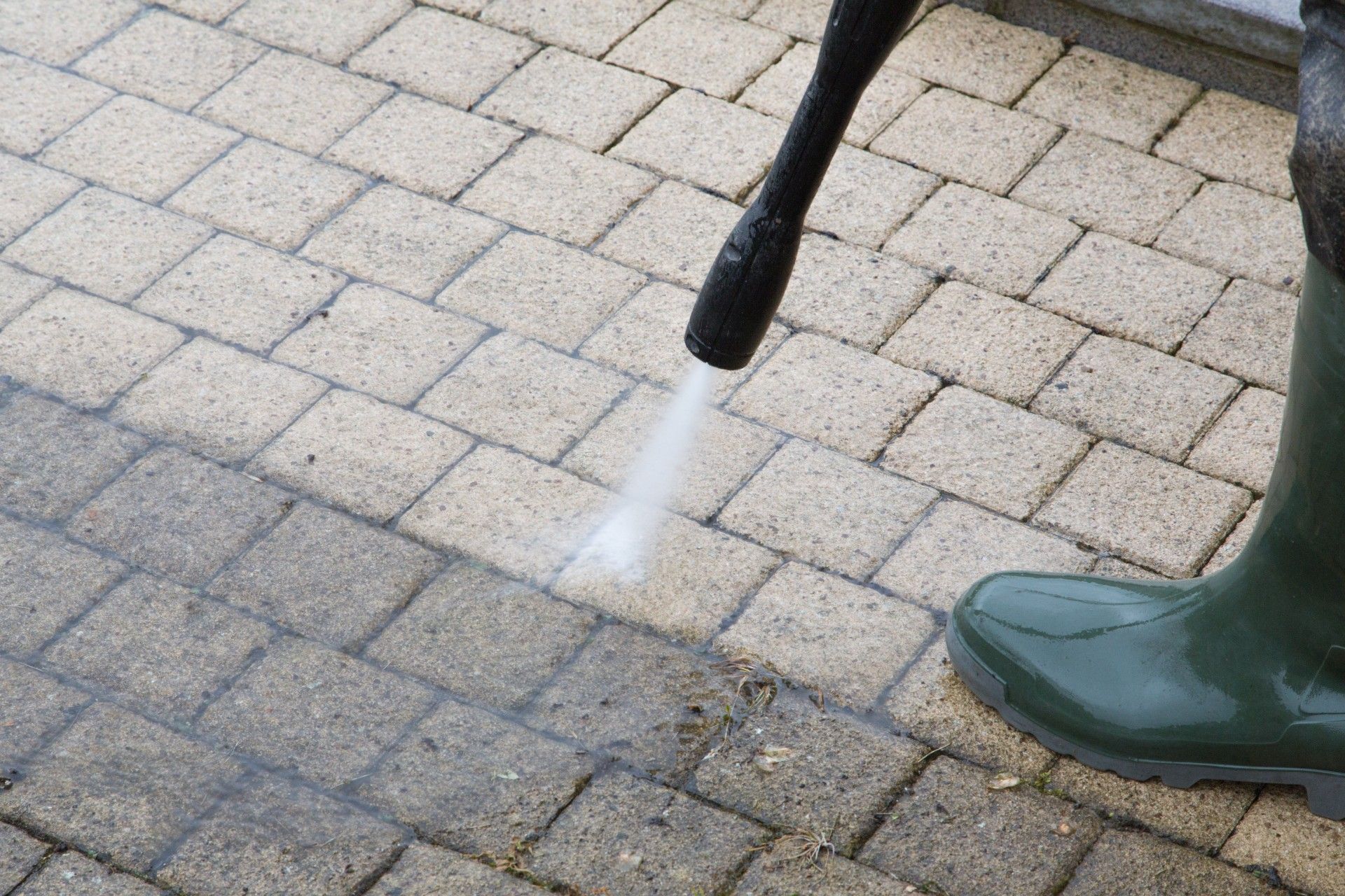 Horse leg with water spray being rinsed on a paved surface, beside a green boot