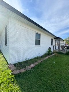 White brick house exterior with a small porch, windows, and green lawn under a blue sky