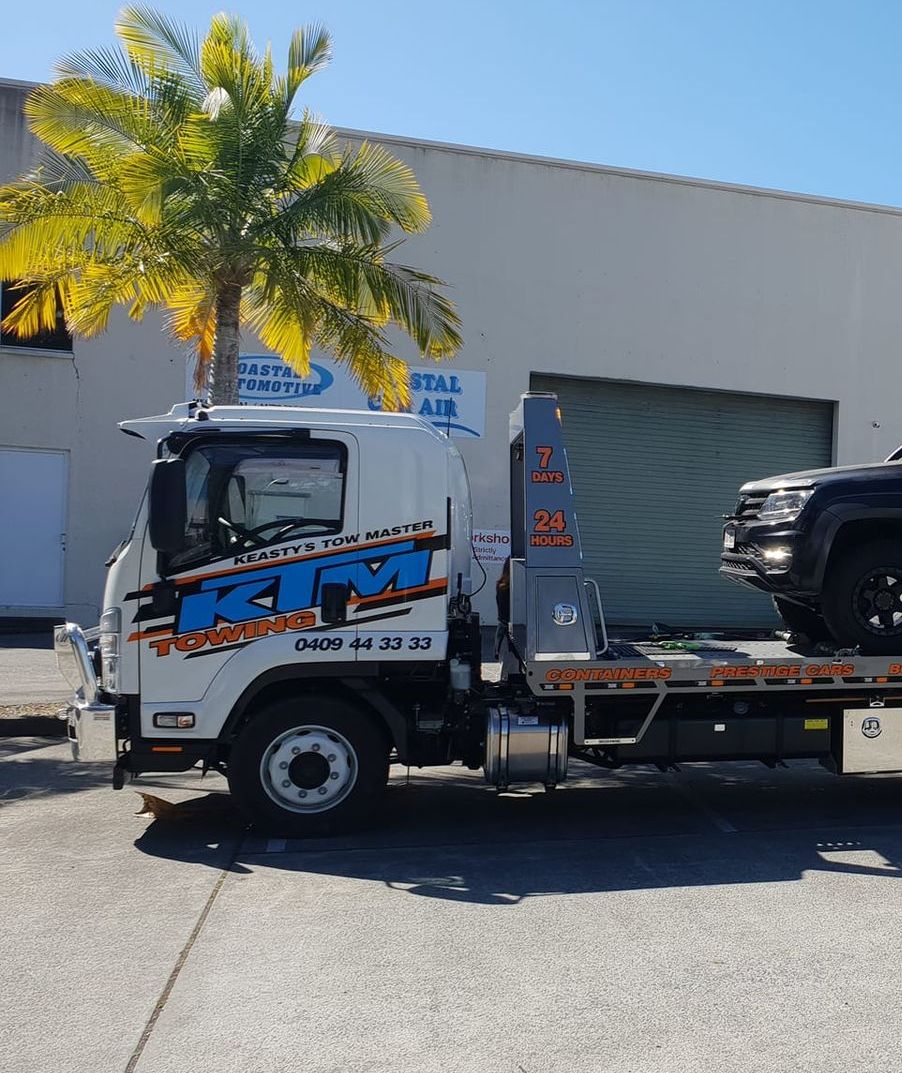 A Tow Truck With A Car On The Back Is Parked In Front Of A Building — KTM Towing In Kempsey, NSW