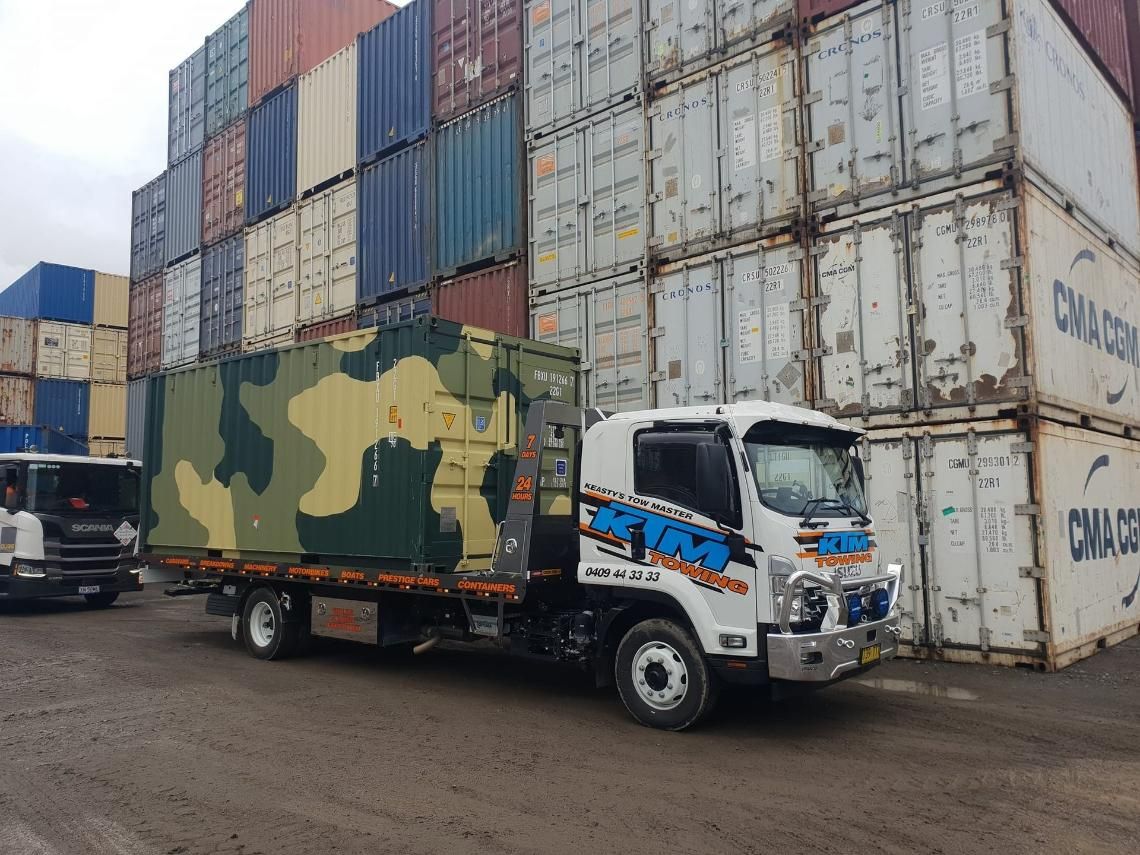 A Truck Is Towing A Container In Front Of A Stack Of Shipping Containers — KTM Towing In Kempsey, NSW