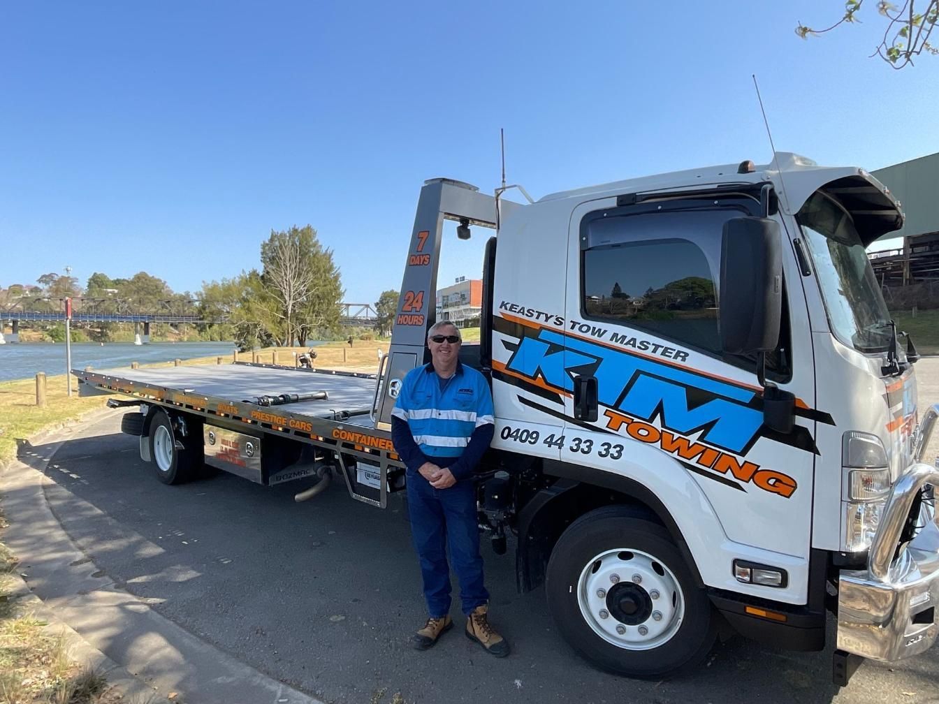 A Man Is Standing In Front Of A Tow Truck — KTM Towing In Kempsey, NSW