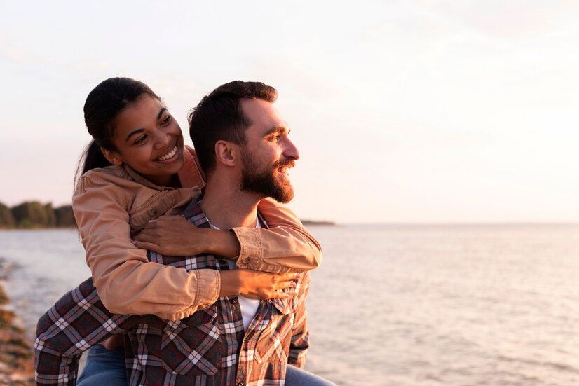A man is carrying a woman on his back at the beach.