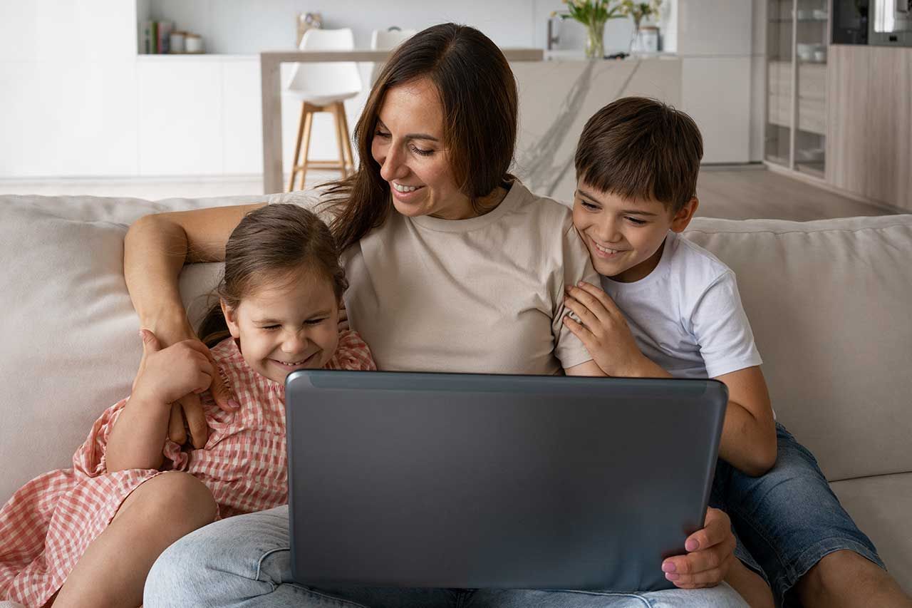A mom and her kids sitting on the couch watching a video from their school