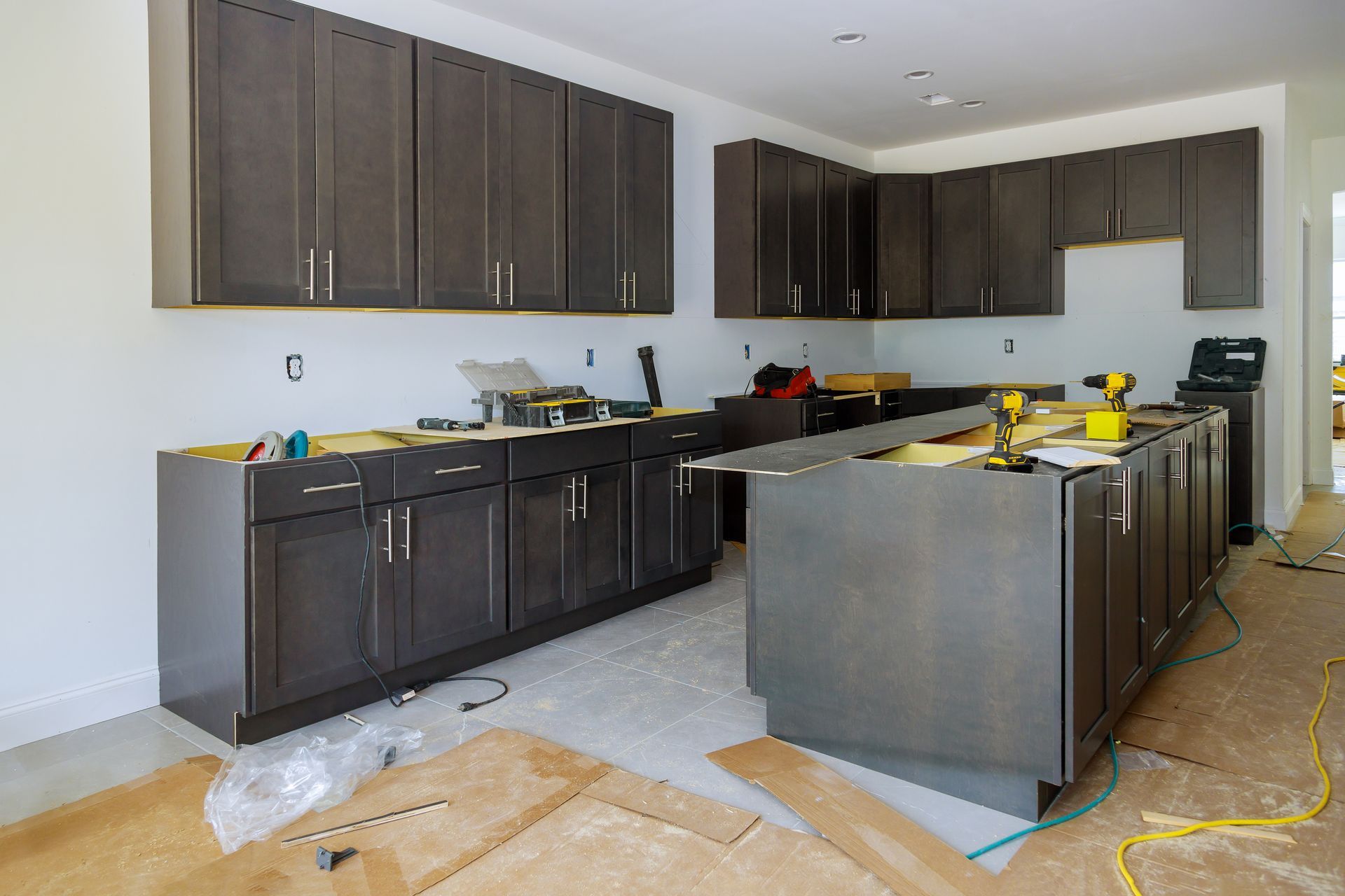Kitchen renovation: Dark brown cabinets being installed. Construction tools and materials visible.