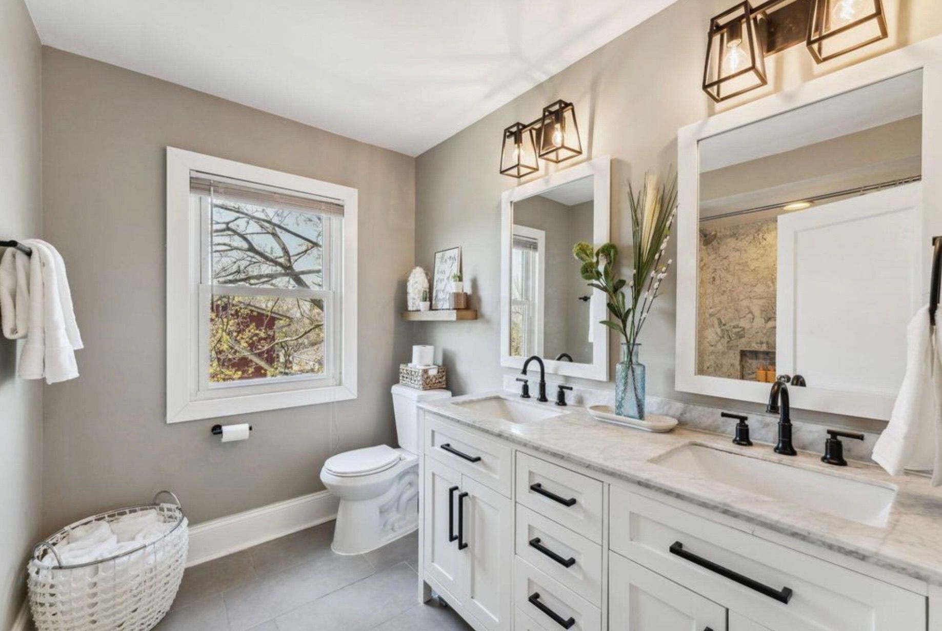 Bright modern bathroom with white vanity, large mirror, window, and neutral decor