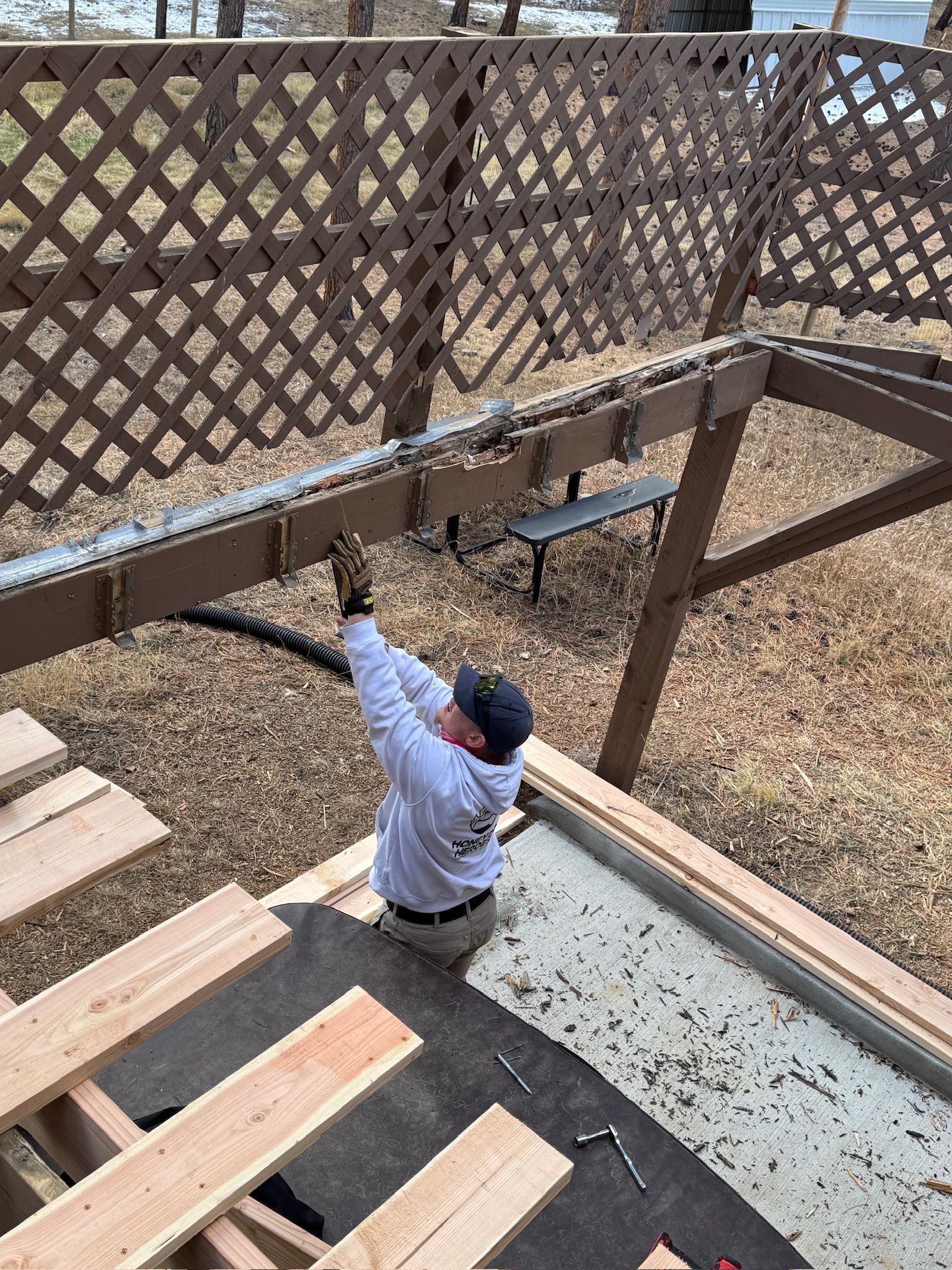 Person on outdoor stairs reaching up to adjust a wire or light under a wooden lattice fence.