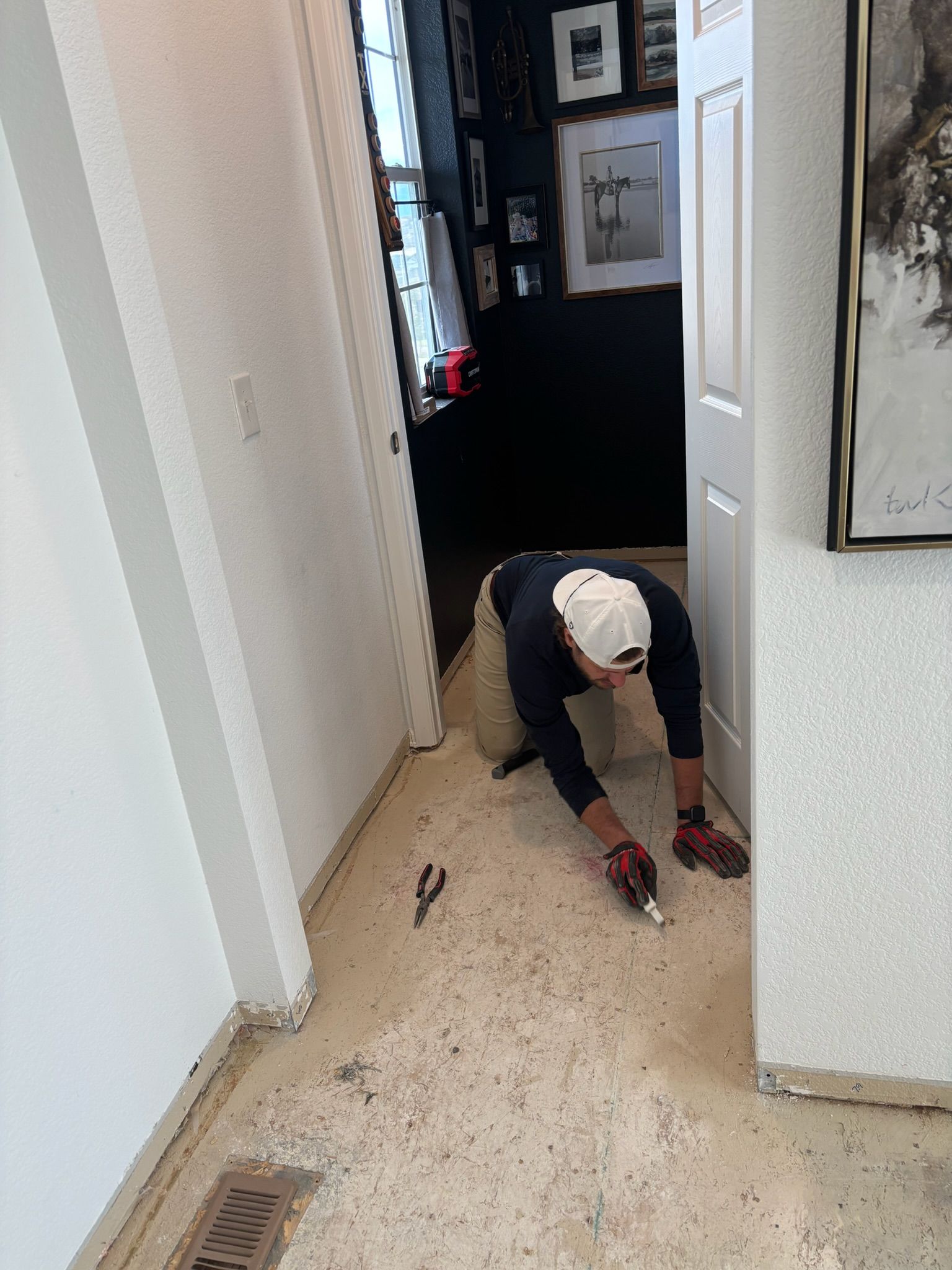 Person kneeling on a hallway floor, working near a wall with tools nearby.