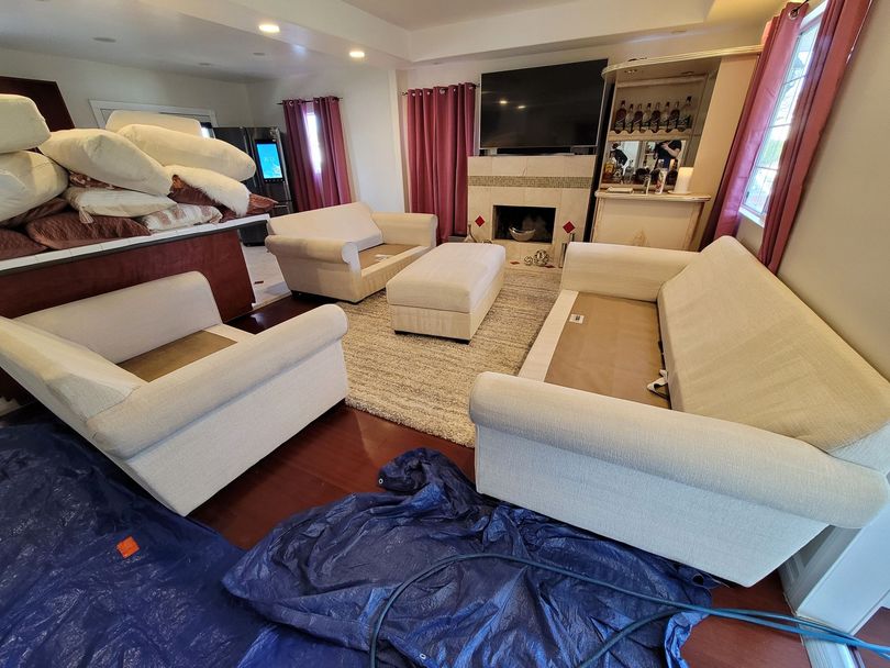 Living room with white sofas, armchairs, fireplace, rug, and TV in a cozy, cluttered interior.