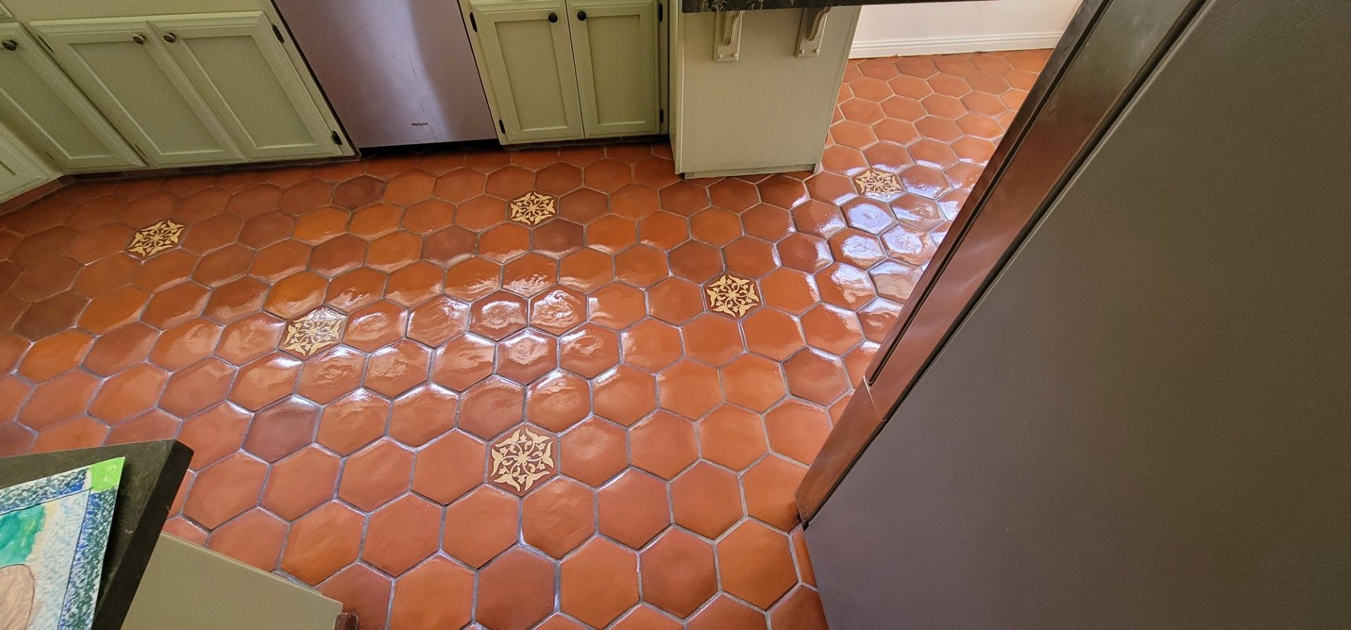Terracotta hex tile floor in a kitchen, with cabinets and a wall along the edges.