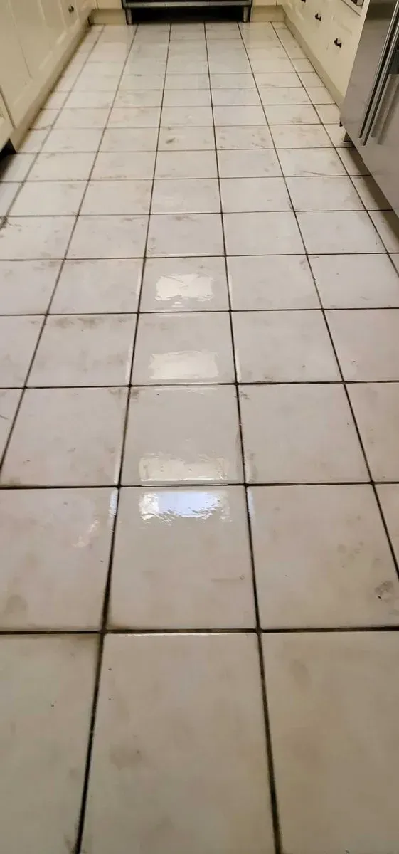 Long white tiled hallway floor with dark grout lines, leading toward a doorway.