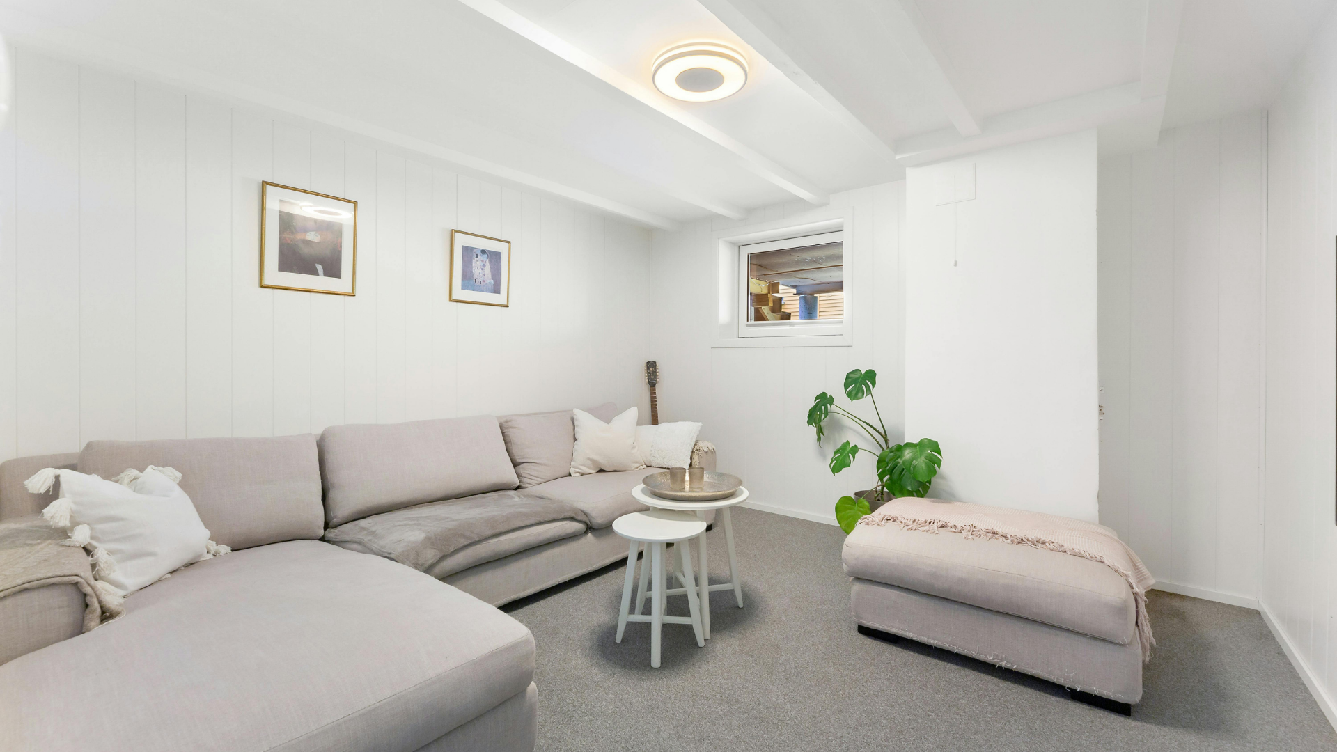Bright modern living room with a gray sectional sofa, small table, and potted plant on a white wall.