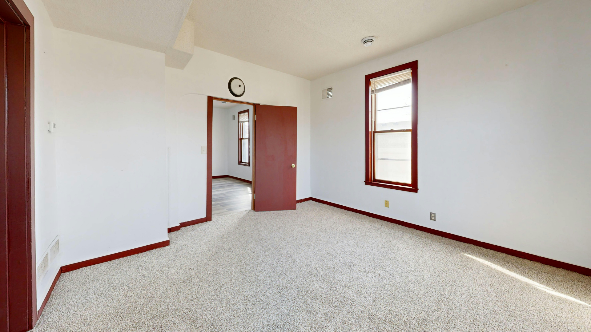 Empty carpeted room with white walls, wood trim, and an open doorway leading to a hall