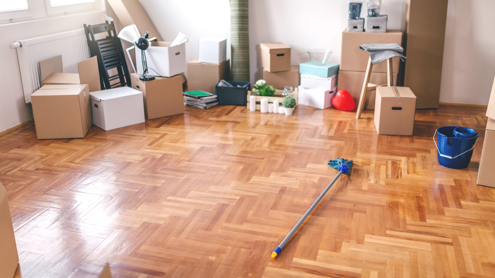 Empty room with hardwood floor, moving boxes, cleaning supplies, and a mop near the center.