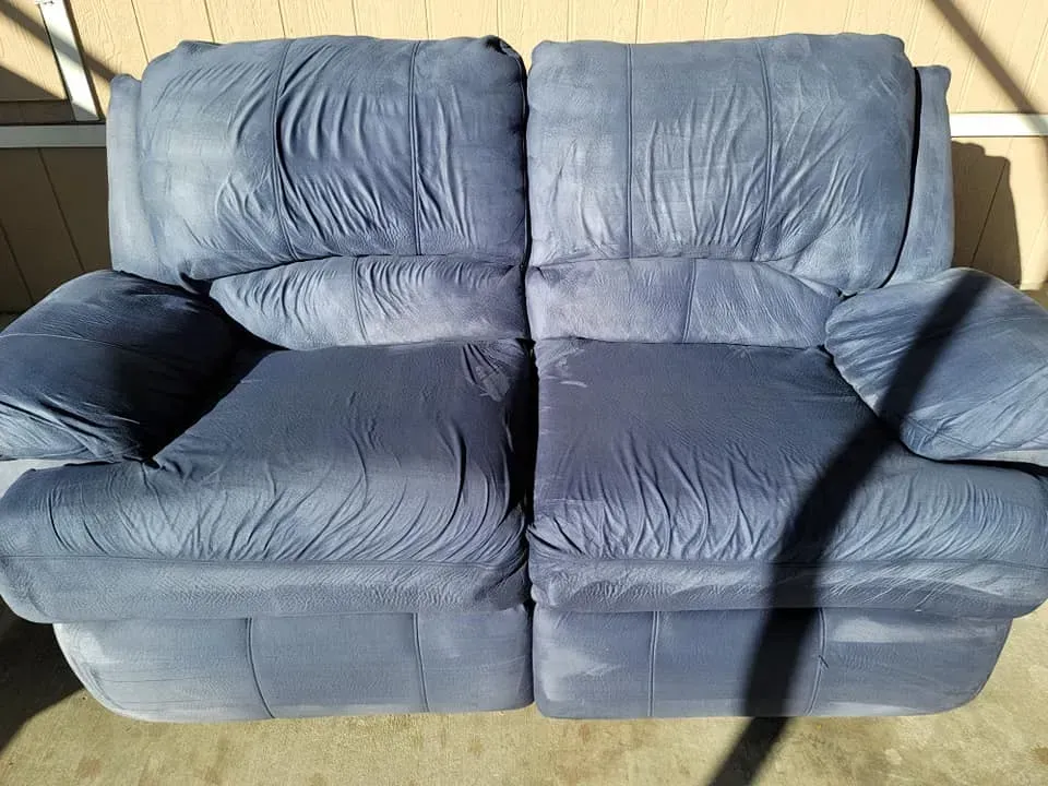Blue two-seat couch with worn, wrinkled cushions against a beige wall