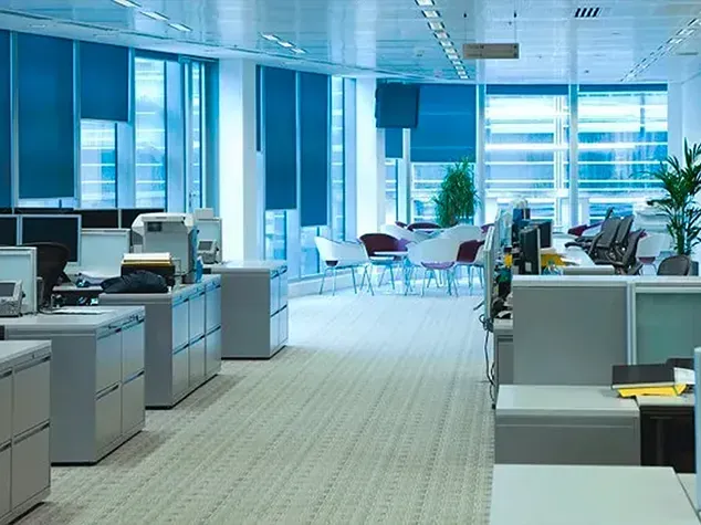 Empty modern office with desks, computers, and bright blue-tinted windows