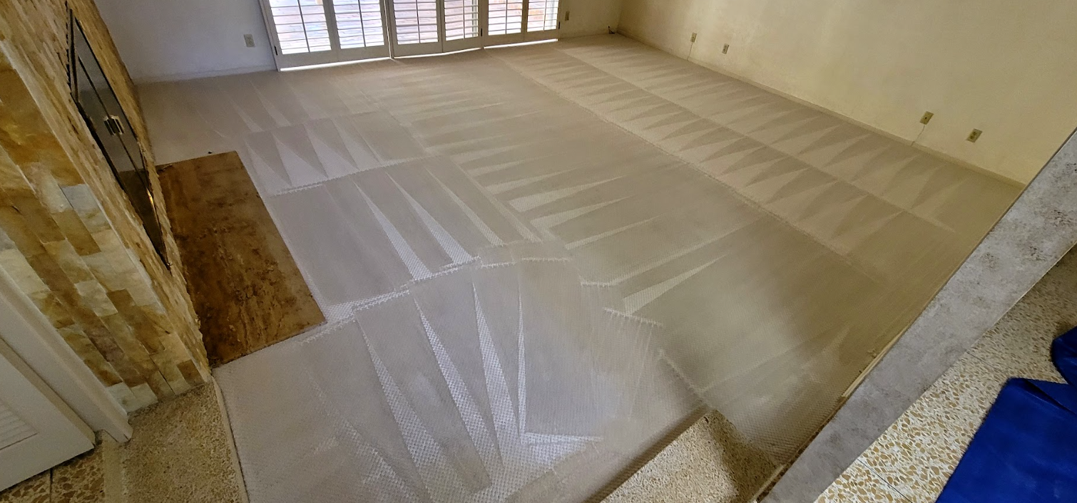 Large room under renovation with plastic sheeting covering the floor and windows at the far end