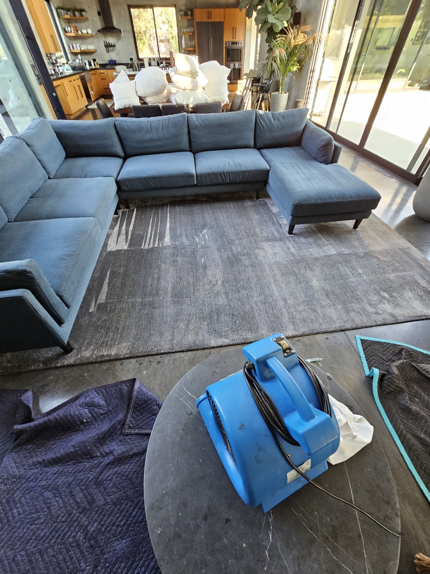 Gray sectional sofa in a sunroom, with a blue bag and dark bag on a round table in the foreground.