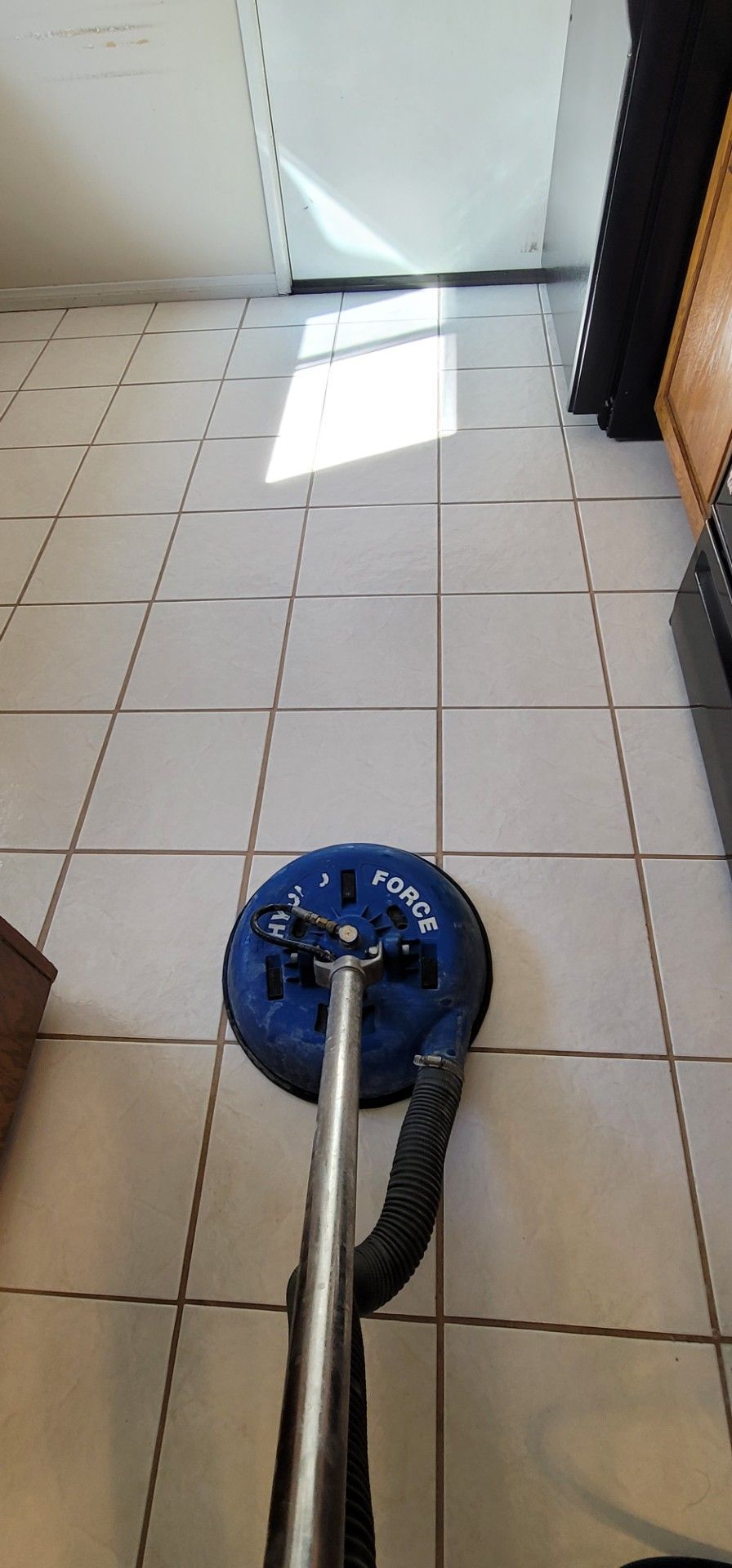 Blue floor buffer on white tiled floor near a sunlit doorway
