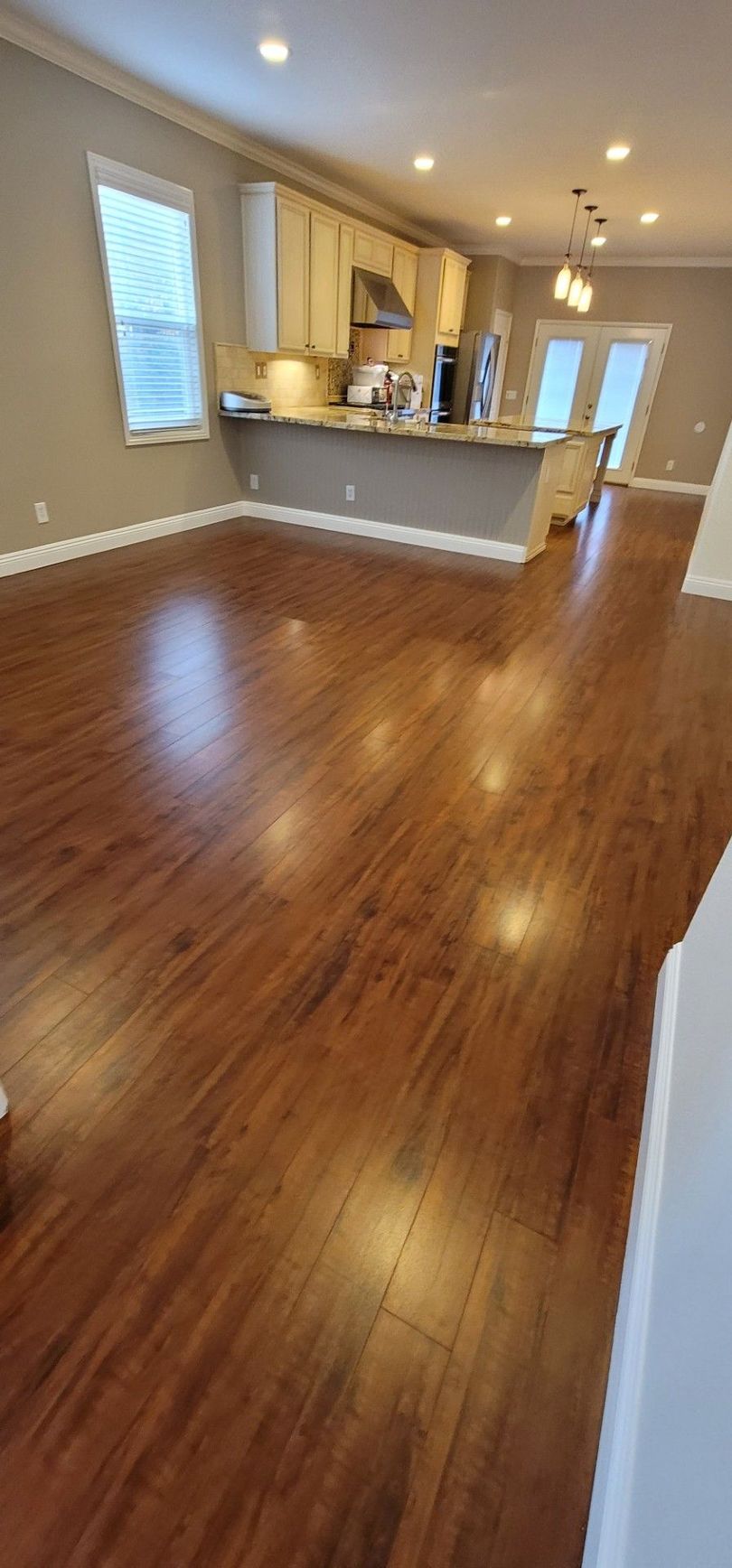 Empty open-plan living room with hardwood floors and a kitchen island in the background