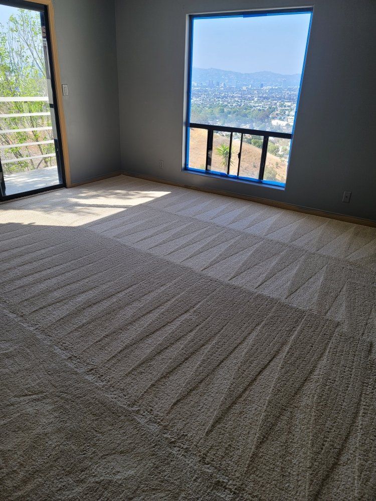 Empty unfurnished room with carpeted floor and two windows overlooking a distant city and hills