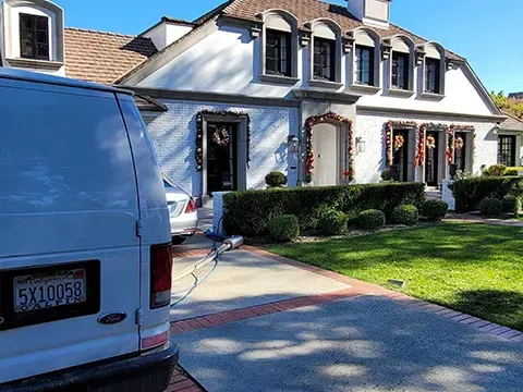 Blue van parked in front of a white house with dormer windows and a manicured lawn