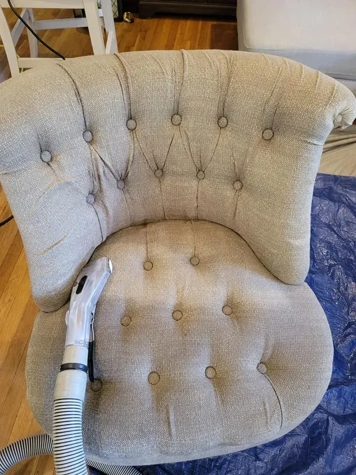Beige tufted armchair with a vacuum hose resting on the seat and arm.