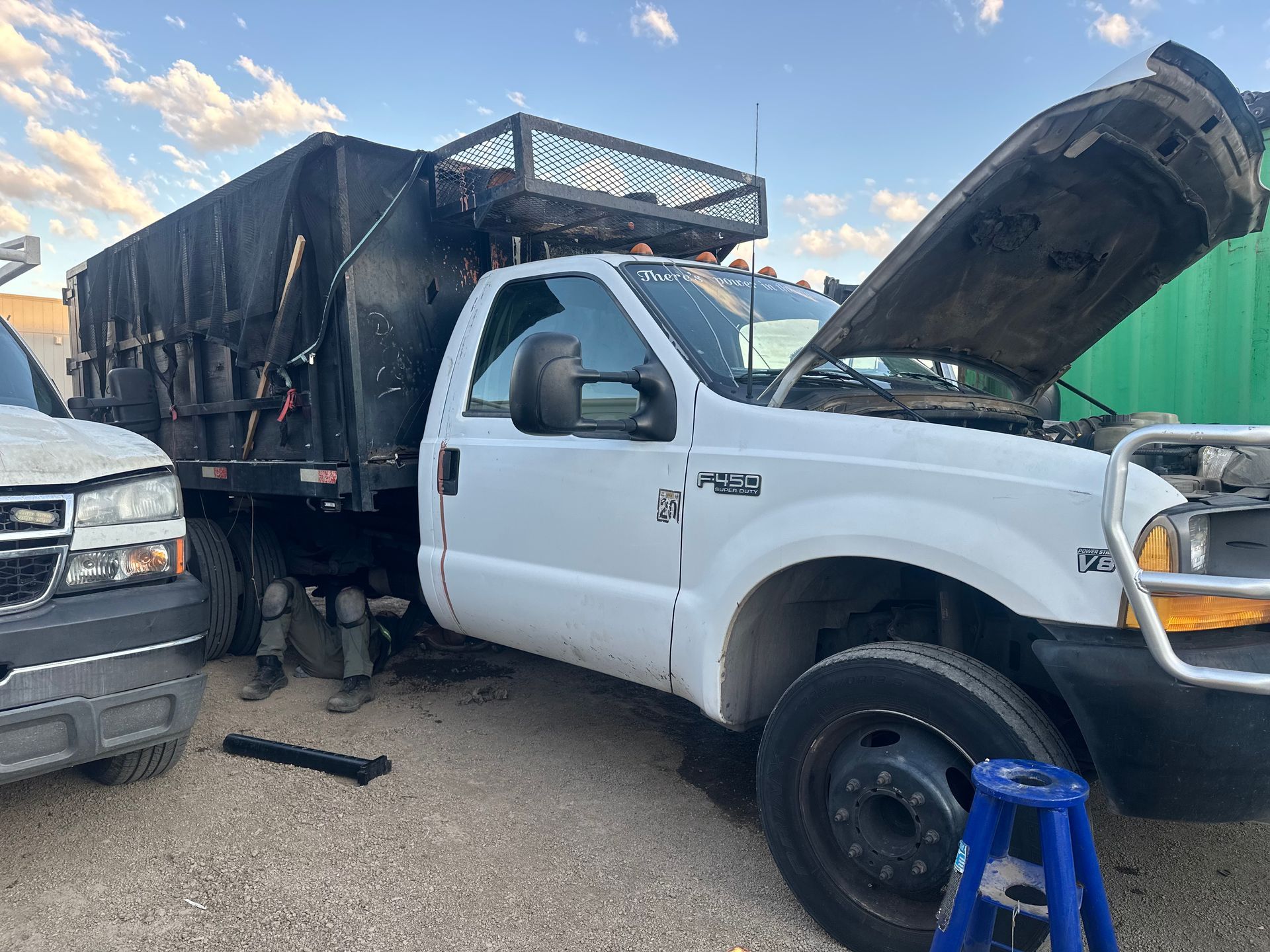 White dump truck with open hood, black bed, next to a white truck.