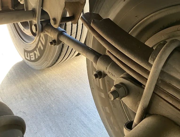 Close-up of a truck’s rear wheel, suspension, and axle on a road.