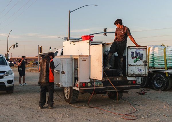 Workers on a utility truck in a roadside lot at dusk, with equipment and cables around them
