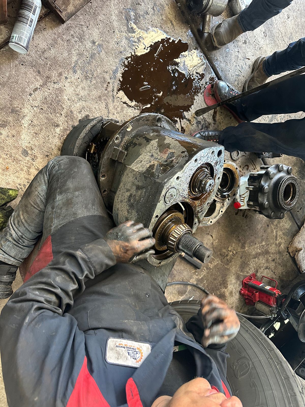 Mechanic working on an open, greasy differential on a shop floor; hands covered in oil.