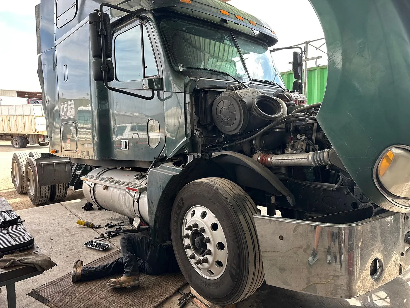 A man is working on a semi truck with the hood open.