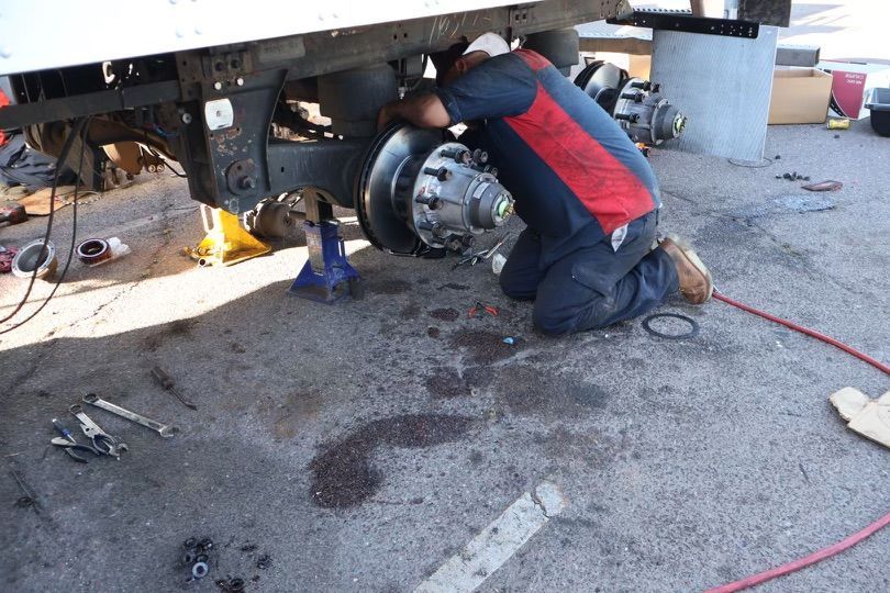 A man is kneeling down under a truck working on it