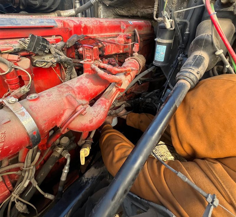 Person working on a red engine in a truck, with visible pipes and wires.
