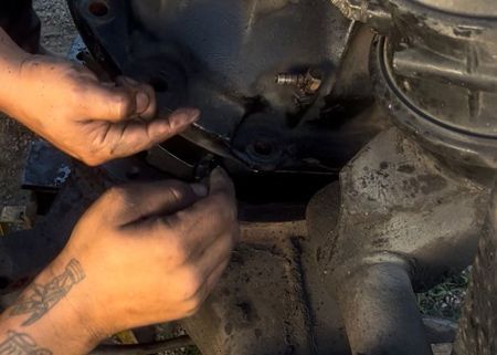 Hands working on a dark, greasy mechanical component, possibly a vehicle differential.