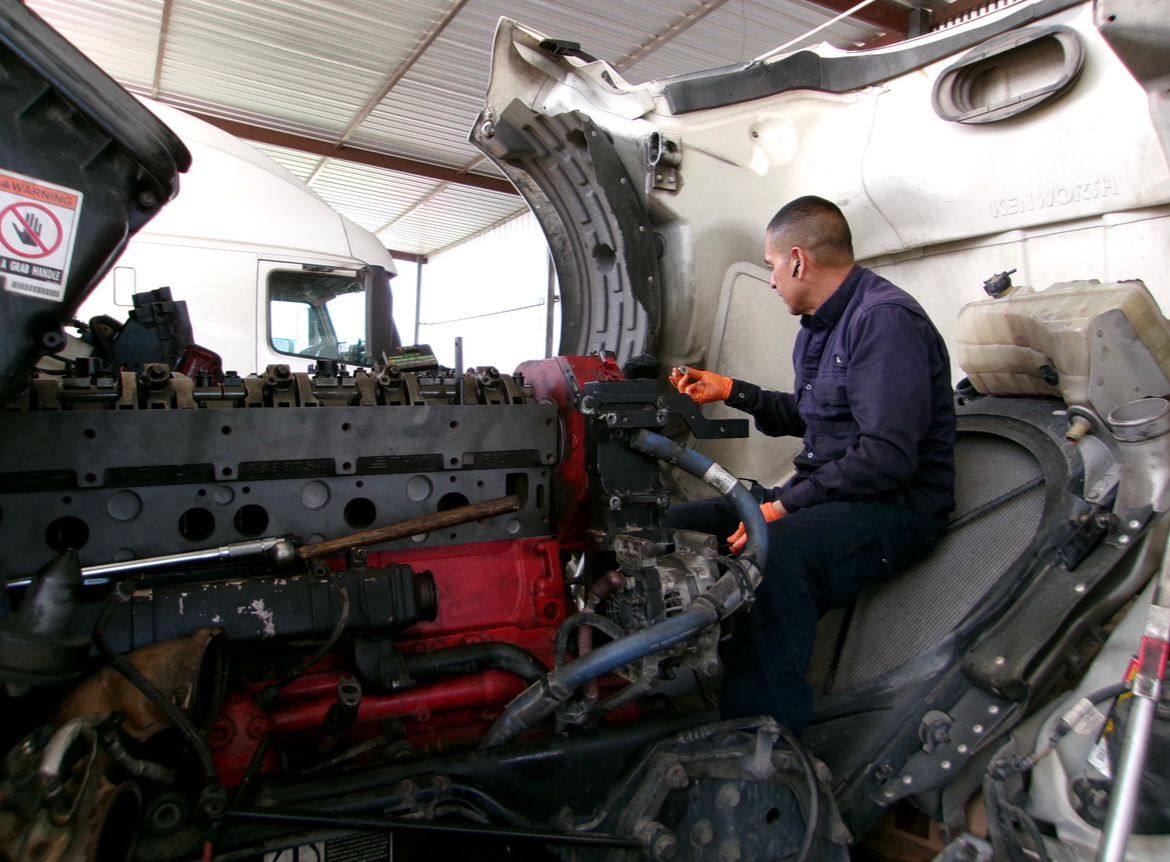 Mechanic working on the exposed engine of a truck in a repair shop.