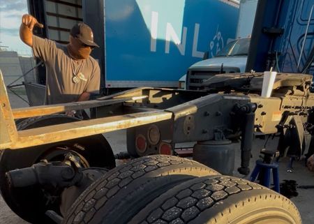 Man working on the undercarriage of a semi-truck; outdoors, daylight.