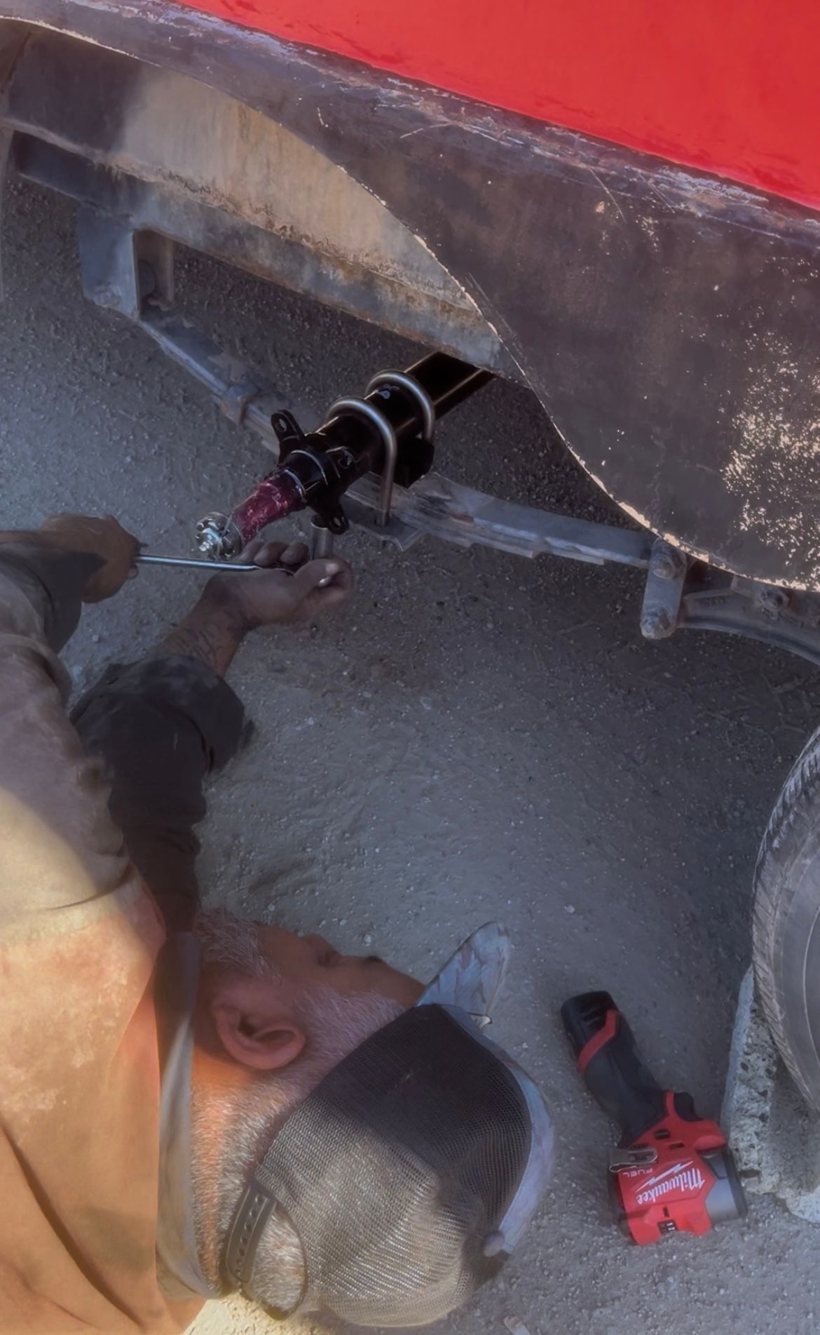 Mechanic working on the underside of a red vehicle. Using a tool, potentially on a suspension part.