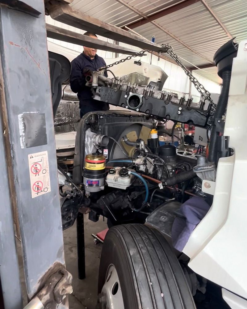 Mechanic working on truck engine, using a hoist inside a repair shop.