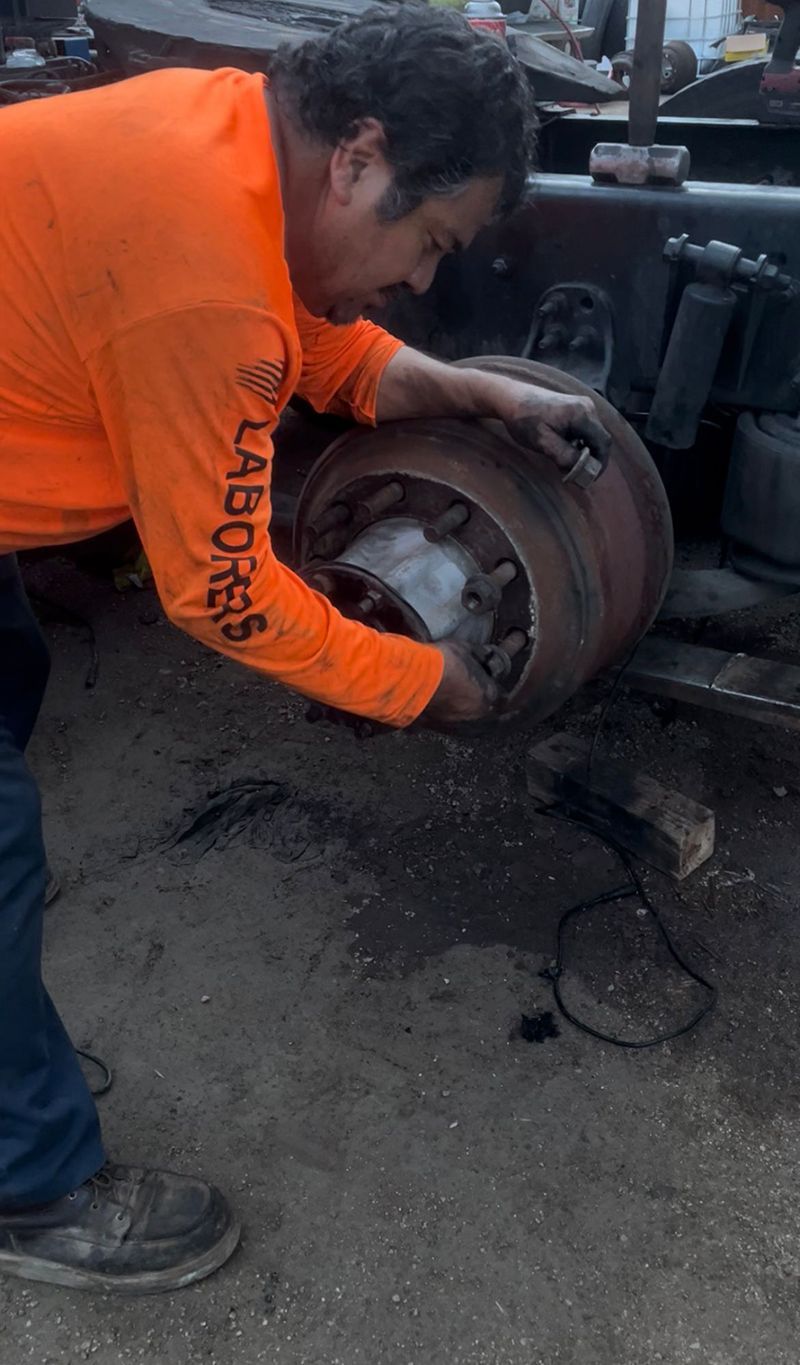 Man in orange shirt working on a truck wheel outdoors, examining it closely.