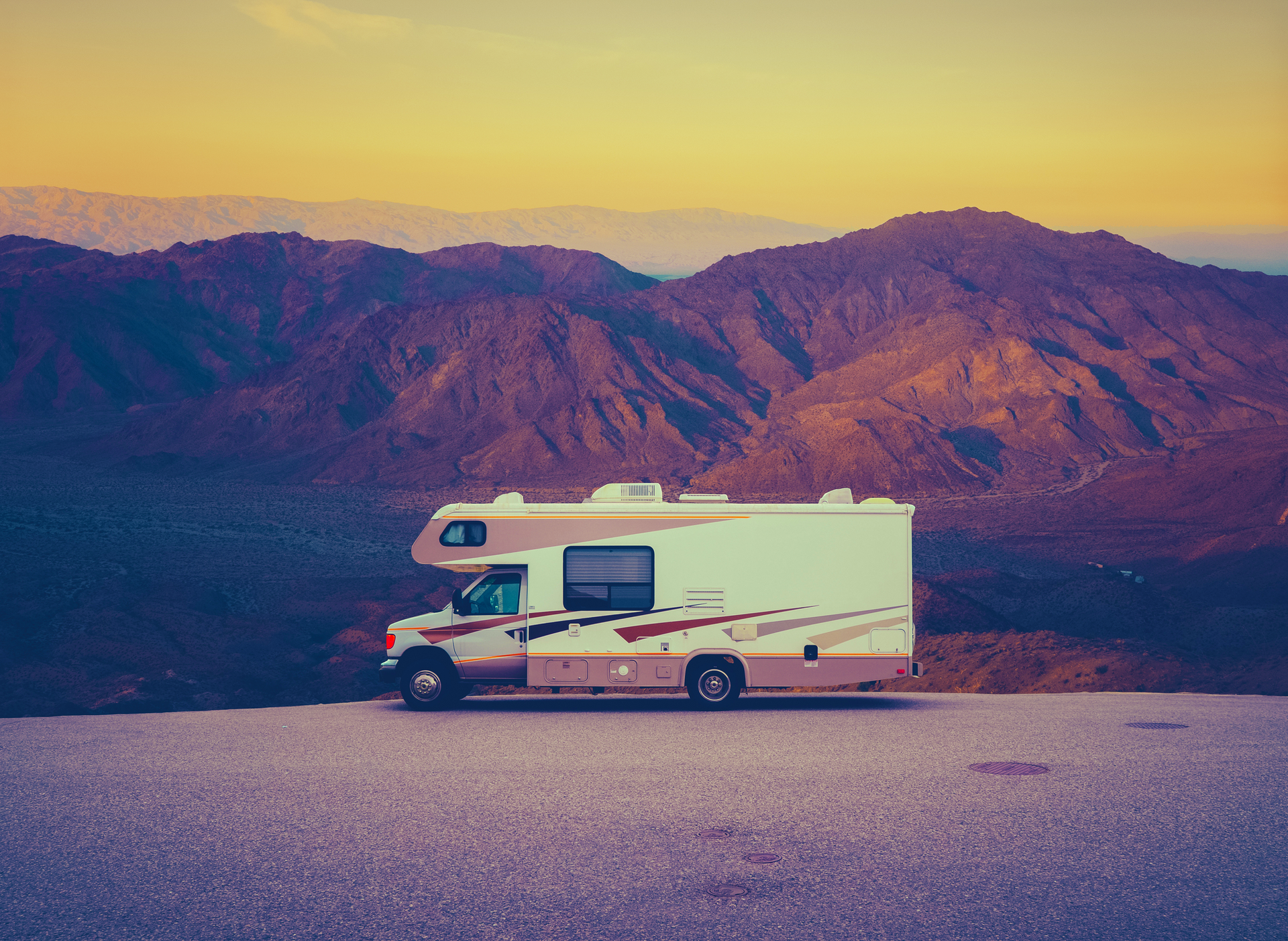 A rv is parked on the side of a road with mountains in the background.