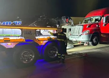 Tow truck at night, recovering a damaged semi-truck. Yellow tow truck lights up the scene.