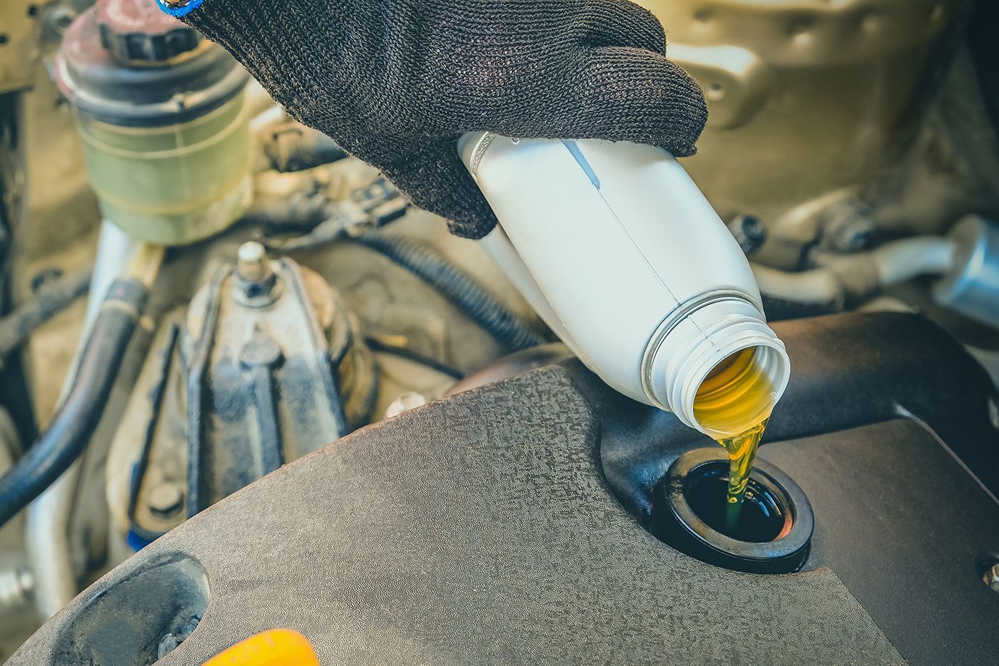 Person pouring oil from a bottle into a car engine, wearing a glove.
