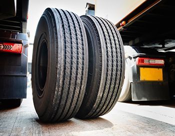 Two truck tires on a gray surface, close up. Black tires with tread, part of a truck.