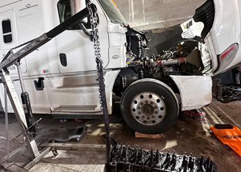 A white semi truck is being repaired in a garage with the hood up.
