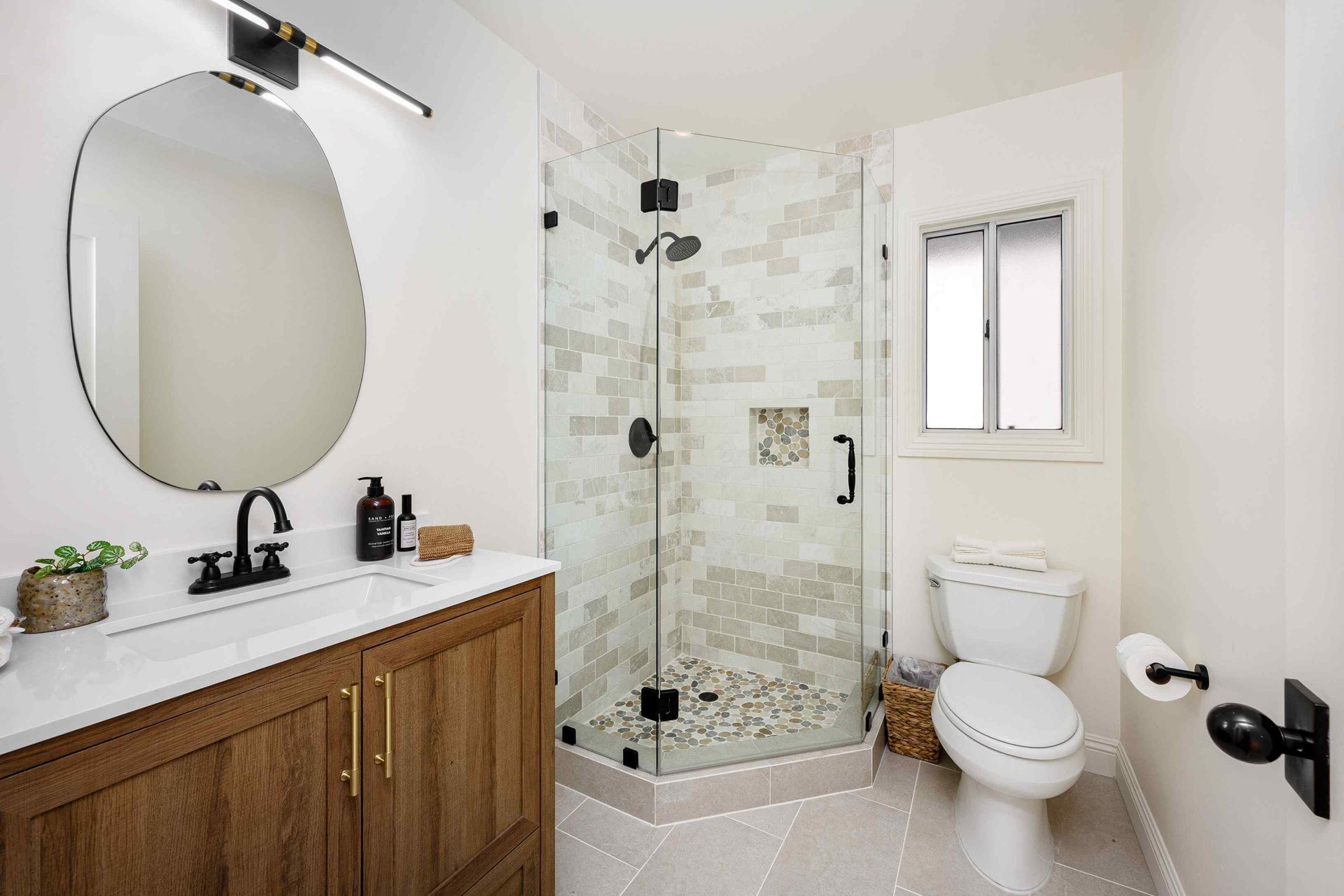 Bathroom with a shower, toilet, and vanity. Neutral tones, wood vanity, and black fixtures.